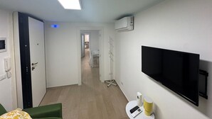 A hotel room with a bed, a TV mounted on the wall, a small table with a lamp, and an air conditioning unit. - FRISELLA (Bari)