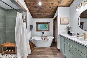 A modern bathroom with a freestanding bathtub, a vanity with a large mirror, and a wooden ceiling. - Modern Mt LeConte Cabin • Hot Tub + Spa Tub (Gatlinburg)