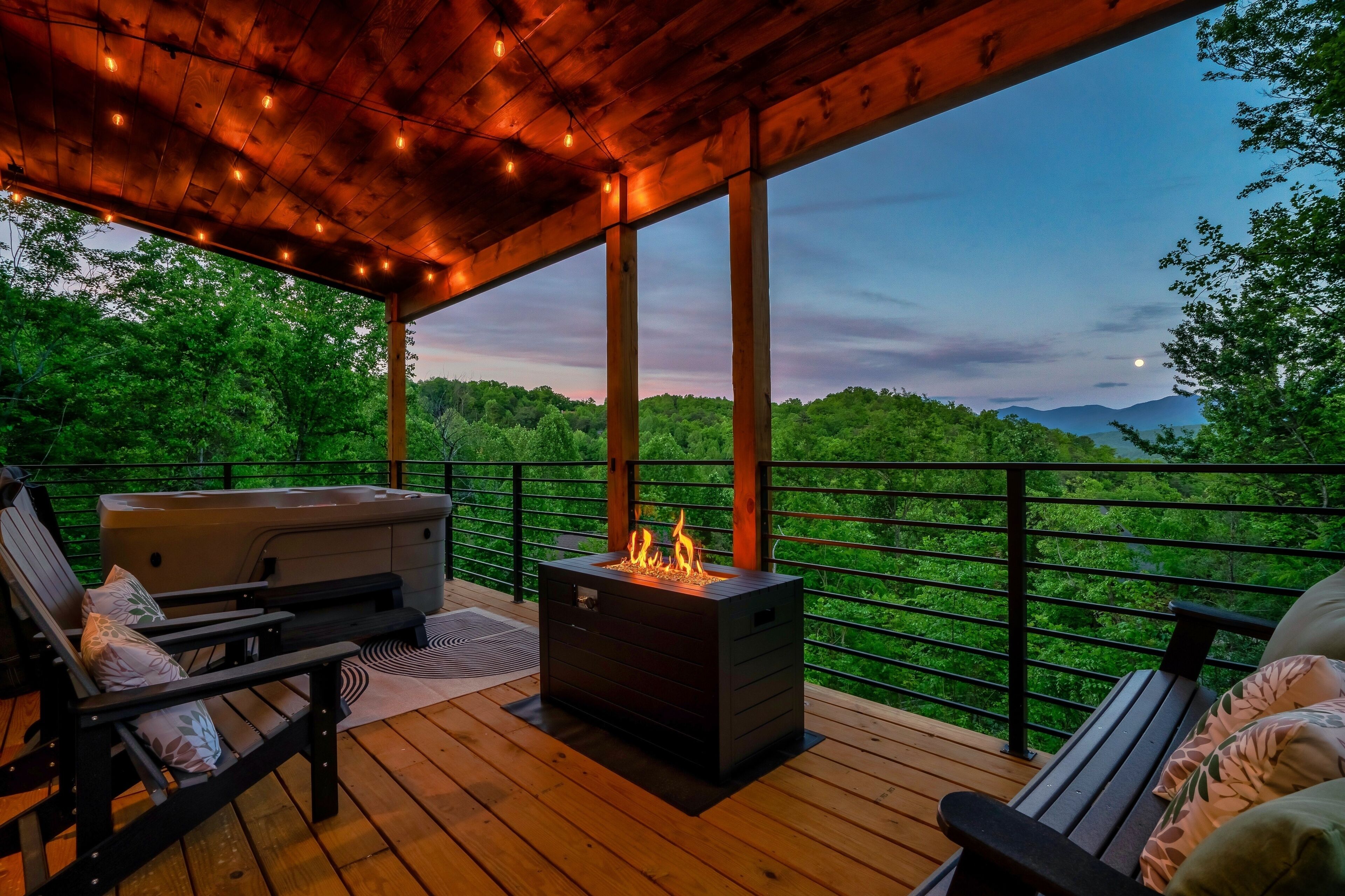A covered deck with a fire feature, seating, and a view of a forested landscape.