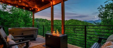 A covered deck with a fire feature, seating, and a view of a forested landscape.