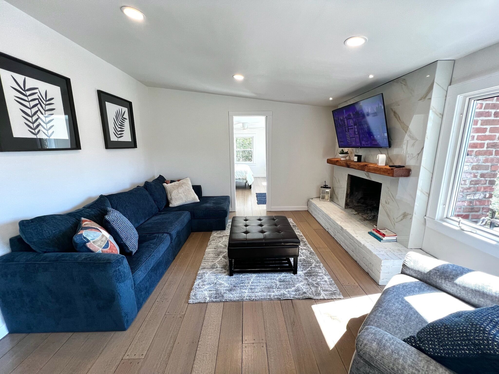 A modern living room with a sectional sofa, a black ottoman, a fireplace, and a TV mounted on the wall.