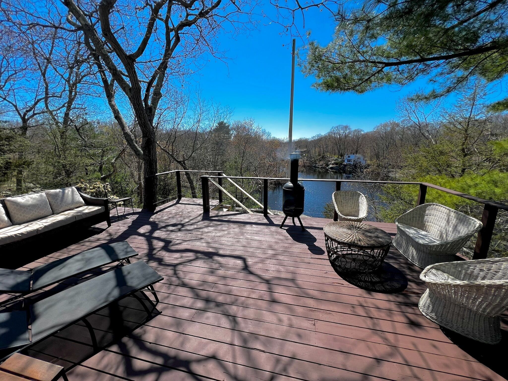 Une terrasse en bois, dotée de mobilier d’extérieur, d’un barbecue et offrant une vue sur un lac entouré d’arbres.