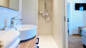Moderni kylpyhuone, jossa on valkoinen pesuallas, peili ja suihku.