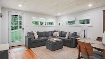 Een moderne woonkamer met een modulaire bank, een houten salontafel, en een eethoek met een tafel en stoelen.