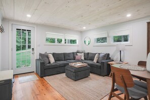 A modern living room with a sectional sofa, a wooden coffee table, and a dining area with a table and chairs. - Cozy Renovated Rustic Cabin Retreat in the Hudson Valley (Ancram)