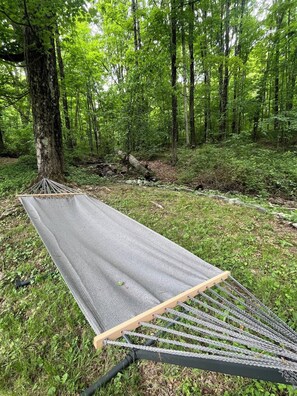 Un hamac installé dans une zone boisée, parmi les arbres et l’herbe.