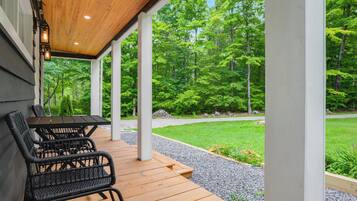 An outdoor patio with a table and chairs, surrounded by a wooden deck and a view of a forest.
