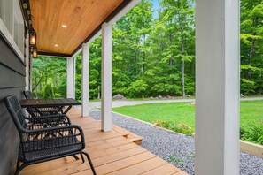 An outdoor patio with a table and chairs, surrounded by a wooden deck and a view of a forest.