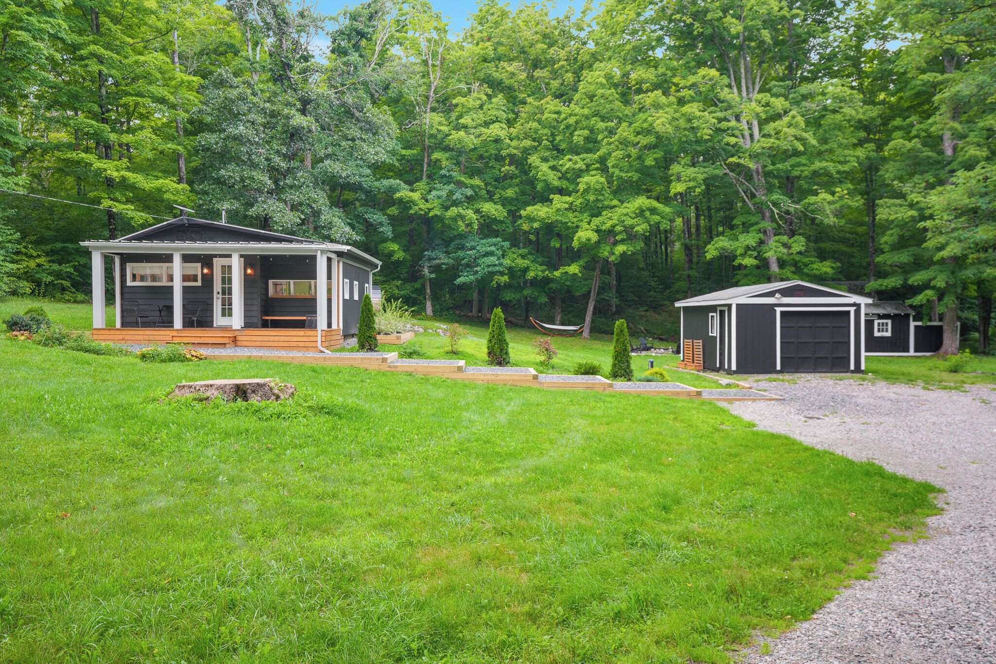 A cabin with a porch and a garage, surrounded by a well-maintained lawn and trees.