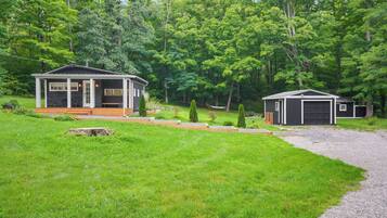 A cabin with a porch and a garage, surrounded by a well-maintained lawn and trees.