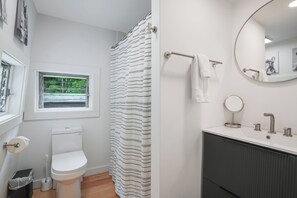 A bathroom with a toilet, a shower curtain, a window, and a sink with a mirror.