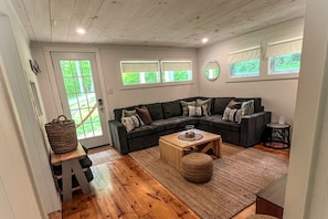 A living room with a sectional sofa, a coffee table, a basket, and a door with a view.