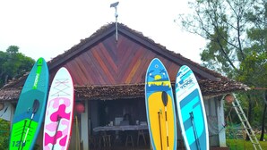 Een gebouw met rieten dak en verschillende surfplanken die er buiten staan.