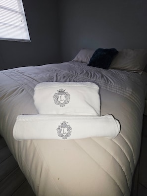 Ein Bett mit weißer Daunendecke und zwei Kissen mit Wappenmuster.