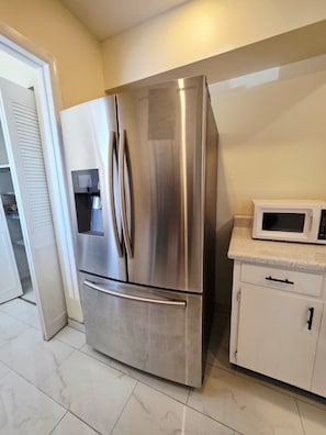 Ein Edelstahl-Kühlschrank mit Wasserspender, einer Mikrowelle und einem weißen Schrank mit Griff.