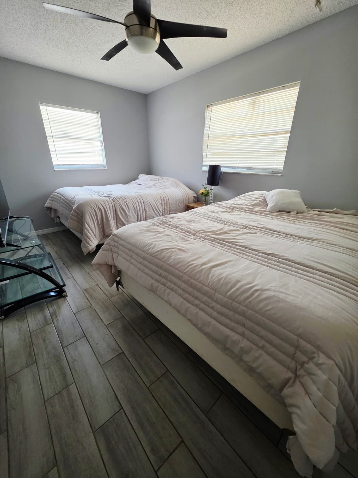 Ein Schlafzimmer mit zwei Betten, einem Deckenventilator und zwei Fenstern mit Jalousien.
