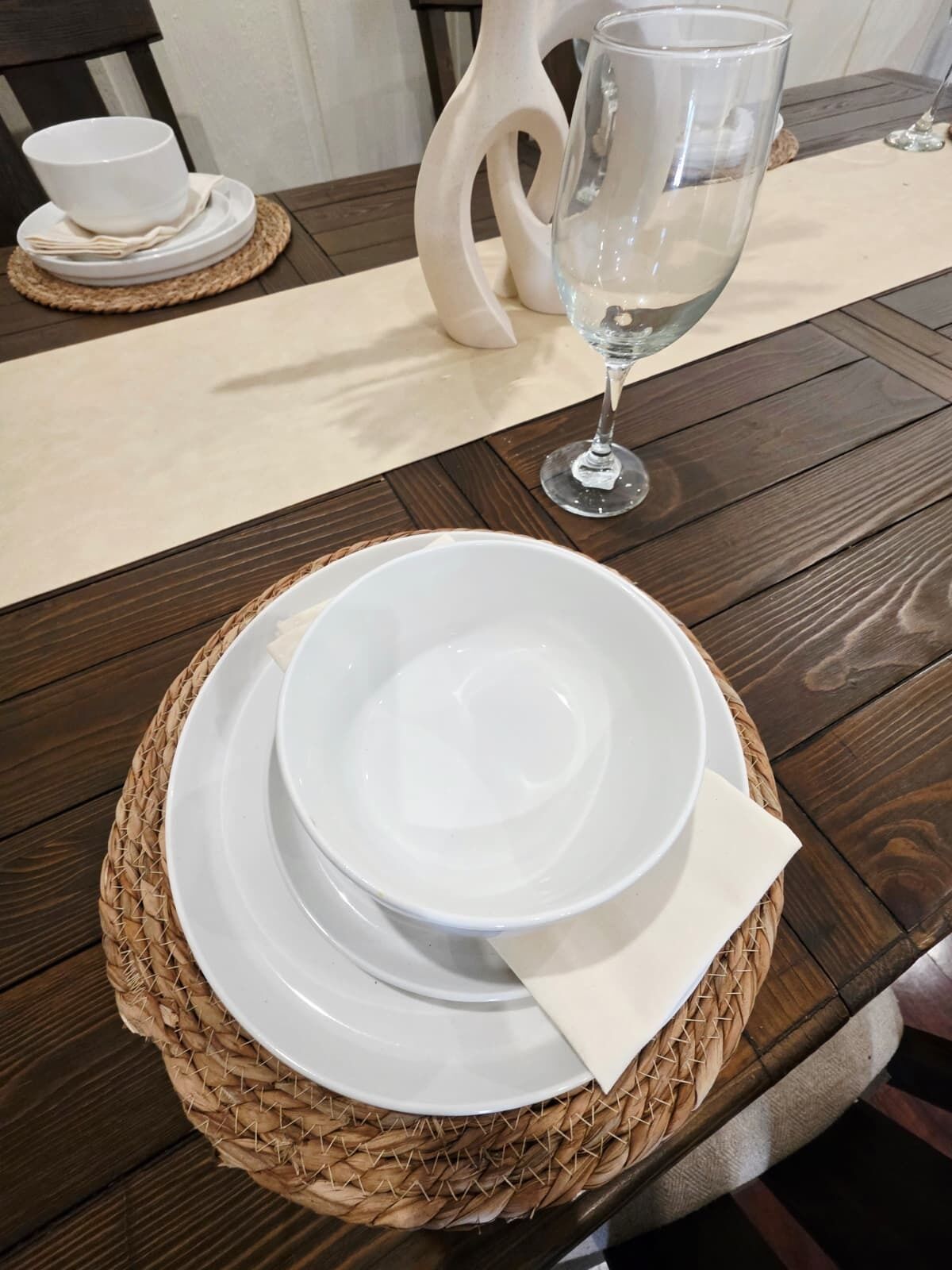 Una mesa con un juego de platos blancos y un vaso sobre un posavasos tejido.
