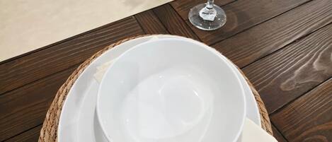 Una mesa con un juego de platos blancos y un vaso sobre un posavasos tejido.
