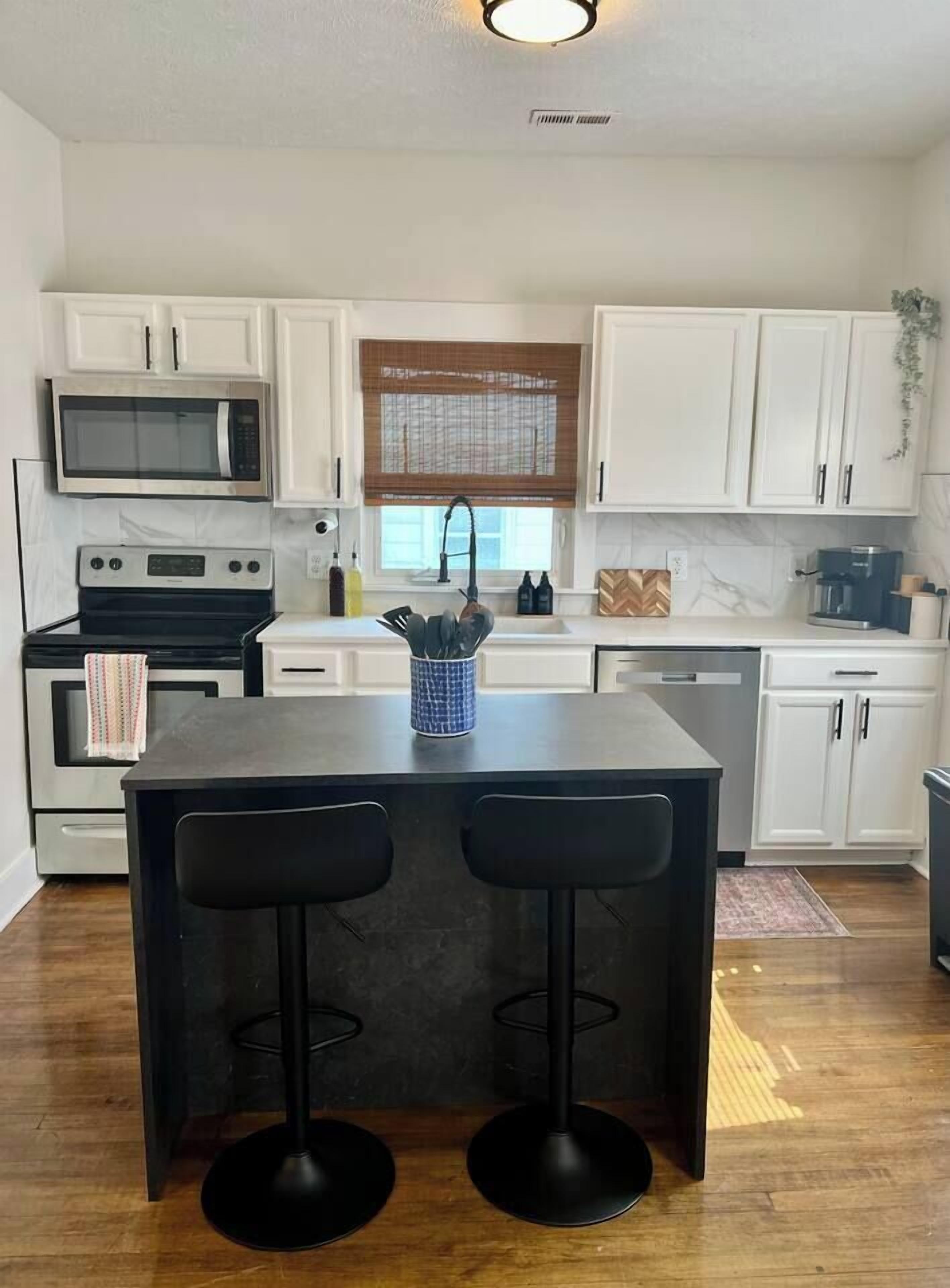 A kitchen with white cabinets, a microwave, an oven, a sink, and two bar stools.