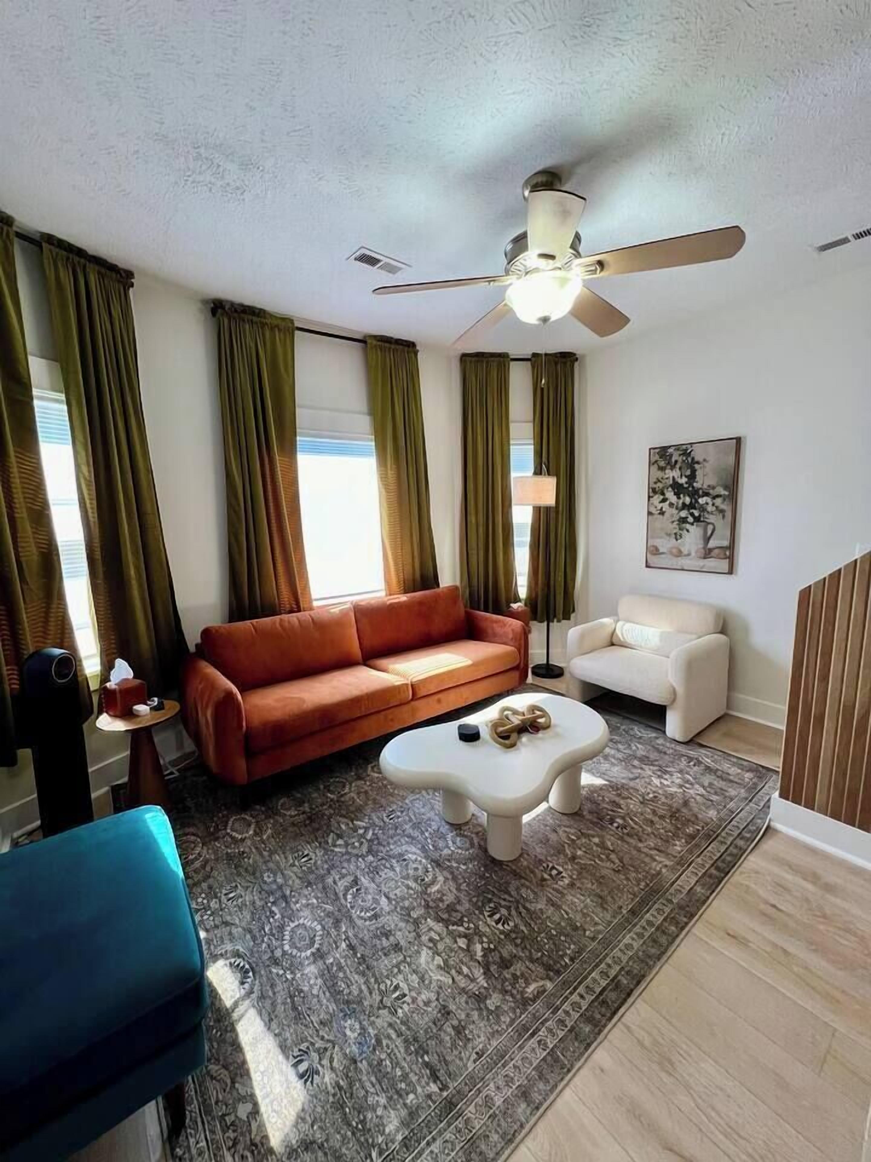 Un salon avec un canapé marron, une table basse blanche, un fauteuil bleu et un ventilateur de plafond.