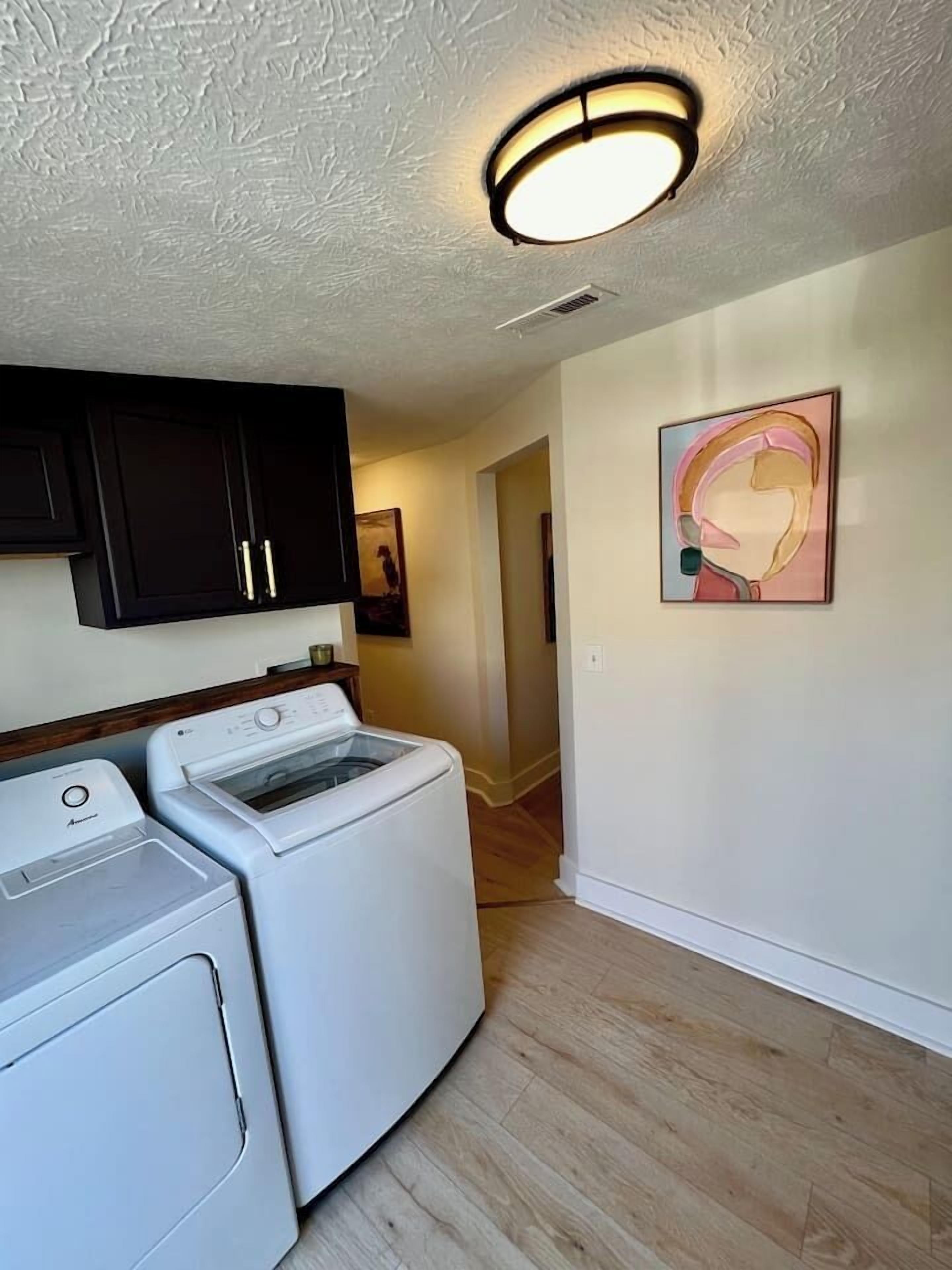 A laundry area with a washing machine and dryer, a ceiling light fixture, and a hallway leading to another room.