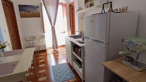 Una cocina compacta con refrigerador, cafetera y comedor con mesa y sillas.