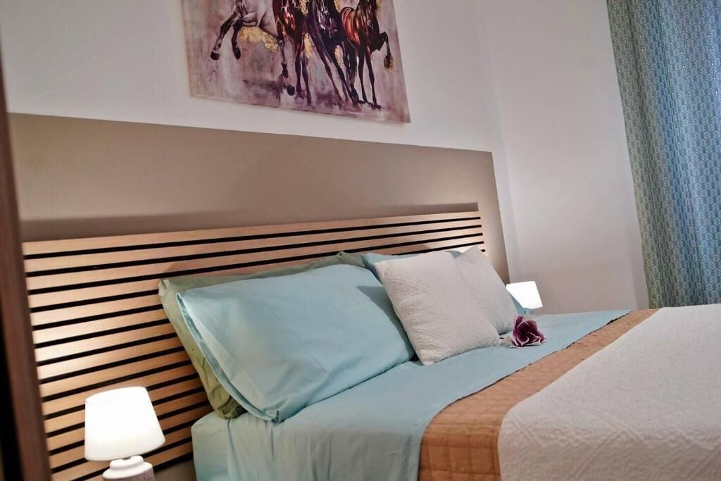 A hotel room with a bed, a headboard, a painting, and a window with curtains.