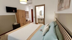 Un dormitorio con cama, televisión, armario de madera, espejo y puerta al baño.