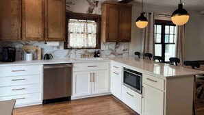 A kitchen with wooden cabinets, a dishwasher, a stove, and pendant lights. - Victoria’s Chamber Fourplex | Rooftop deck and Zoo (Omaha)