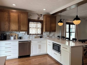 A kitchen with wooden cabinets, a dishwasher, a stove, and pendant lights.