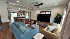A living room with a blue sofa, beige armchair, and a television. - Victoria’s Chamber Fourplex | Rooftop deck and Zoo (Omaha)