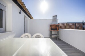 A patio with a white table and chairs, a brick oven, and a white wall.