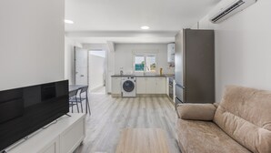 A modern apartment with a flat-screen TV, a sofa, a washing machine, and a kitchen area. - Holiday Home 'Kaki 5' with Private Pool, Wi-Fi and Air Conditioning (Barrio Nuevo)