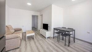 A modern living room with a sofa, a coffee table, a TV on a white cabinet, and a dining area with a table and chairs. - Holiday Home 'Kaki 5' with Private Pool, Wi-Fi and Air Conditioning (Barrio Nuevo)