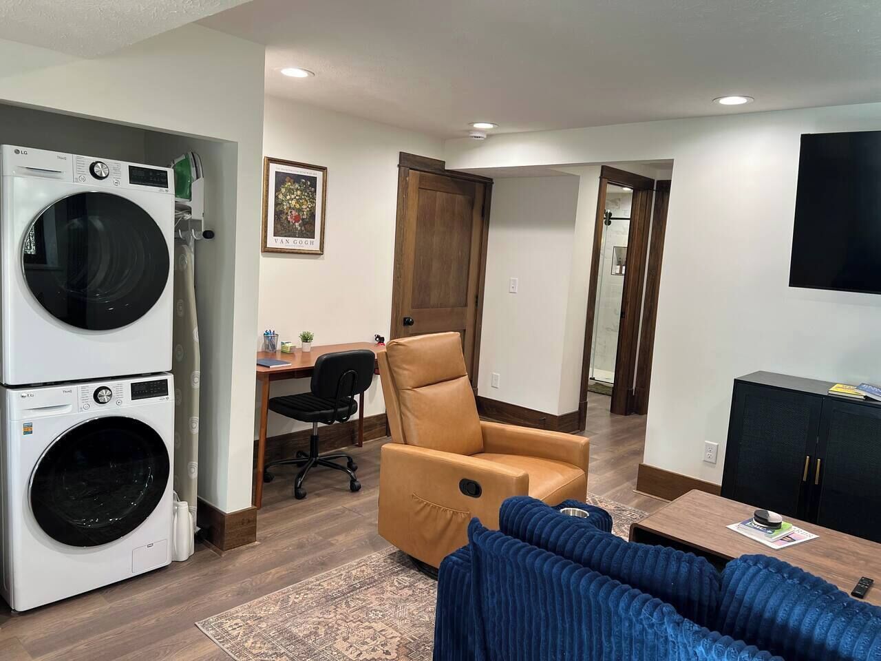 A compact living space with a washing machine, a recliner, a desk with a chair, and a TV.