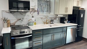 A kitchen with a built-in oven, microwave, and dishwasher, with marble backsplash and wooden flooring. - The Candlelight Cellar on 10th | Fourplex (Omaha)