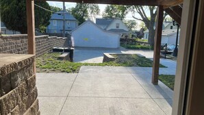 A covered outdoor area with a concrete floor, stone steps, and a view of residential houses in the background. - The Candlelight Cellar on 10th | Fourplex (Omaha)