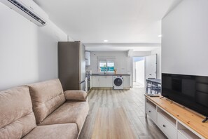 A modern apartment with a sofa, a TV, a kitchen, and a washing machine. - Holiday Home 'Villa Kaki 4' with Private Pool, Wi-Fi and Air Conditioning (Barrio Nuevo)