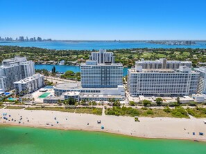 A high-rise hotel with multiple floors, a beach in the foreground, and a city skyline in the background. - 1701 - Studio Ocean Front Free Parking Pool 4 pers (Miami Beach)