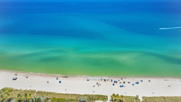 Uma praia com águas azul-claras, areal arenoso e vários guarda-sóis.