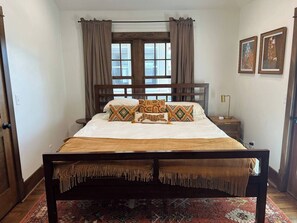 Ein Schlafzimmer mit einem großen Bett, Vorhängen, einem Nachttisch, einer Lampe und zwei gerahmten Bildern an der Wand.