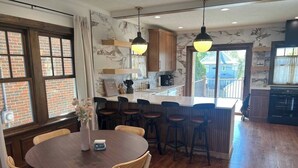 Een keuken met houten kastjes, een centraal eiland, barkrukken en een eettafel met stoelen.