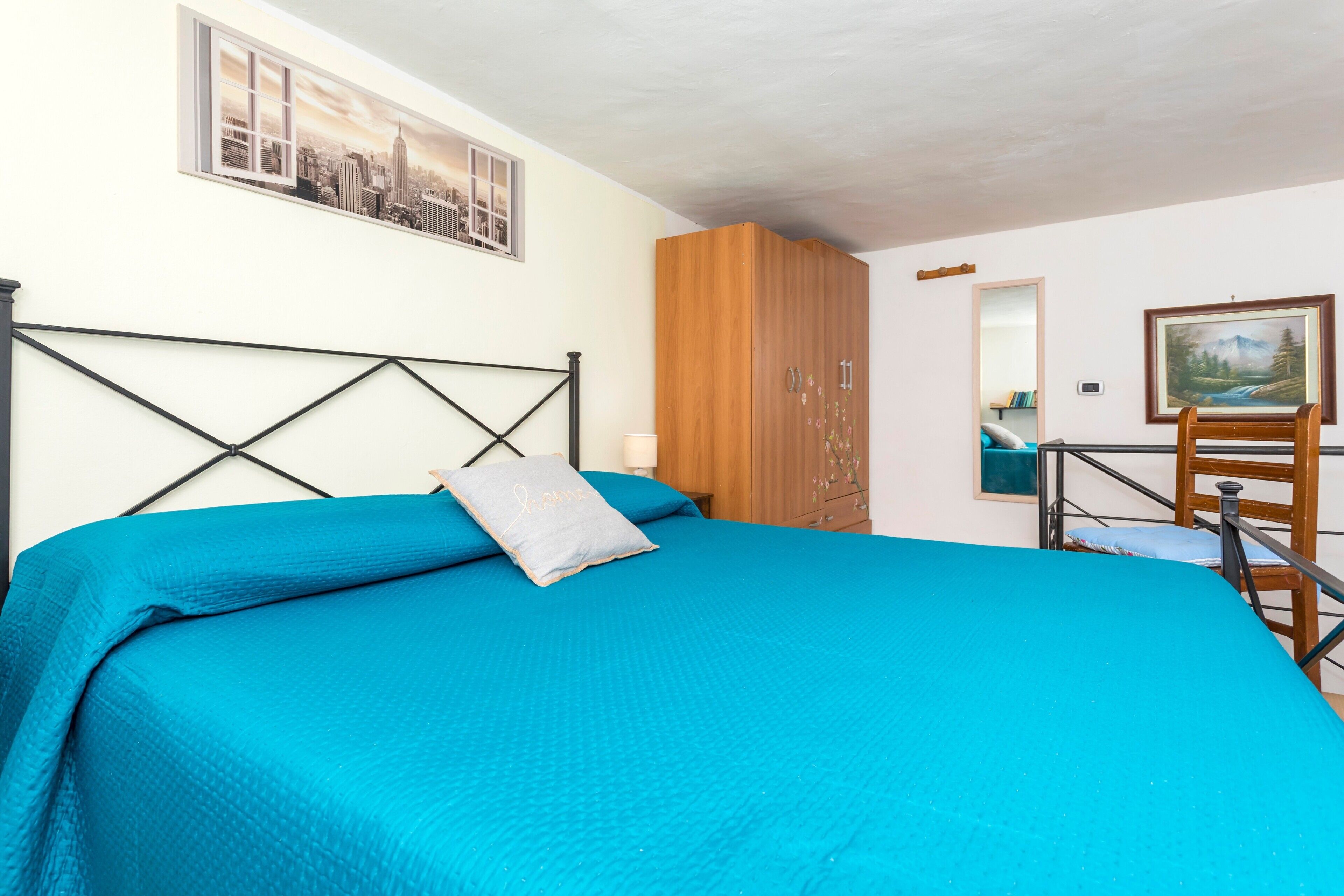 Ein Schlafzimmer mit einem Bett, einem Holzschrank, einem Schreibtisch mit Stuhl, einem Fenster und einem Bild an der Wand.
