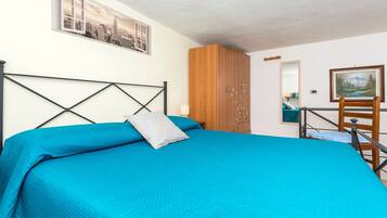 Ein Schlafzimmer mit einem Bett, einem Holzschrank, einem Schreibtisch mit Stuhl, einem Fenster und einem Bild an der Wand.