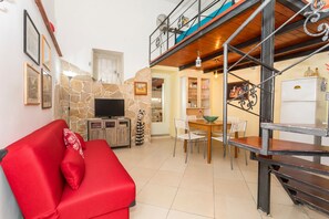 Ein Wohnzimmer mit rotem Sofa, Kamin aus Stein, Fernseher und einem Essbereich mit Stühlen und Tisch.