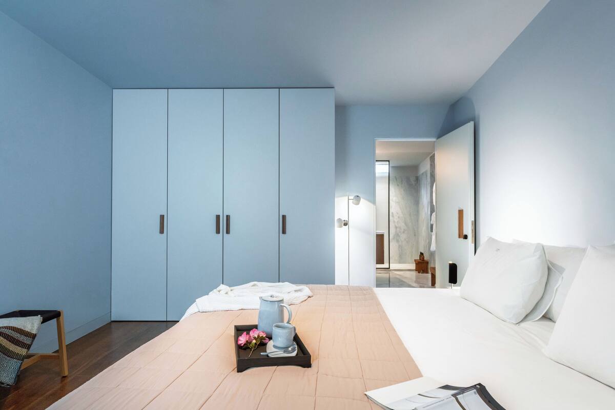 Ett modernt hotellrum med en stor säng, en garderob och ett brickbord med en tekanna och blommor.