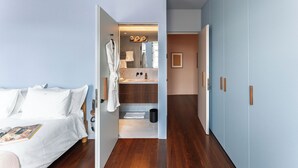 A modern hotel room with a bed, a bathroom with a mirror, and a wardrobe.