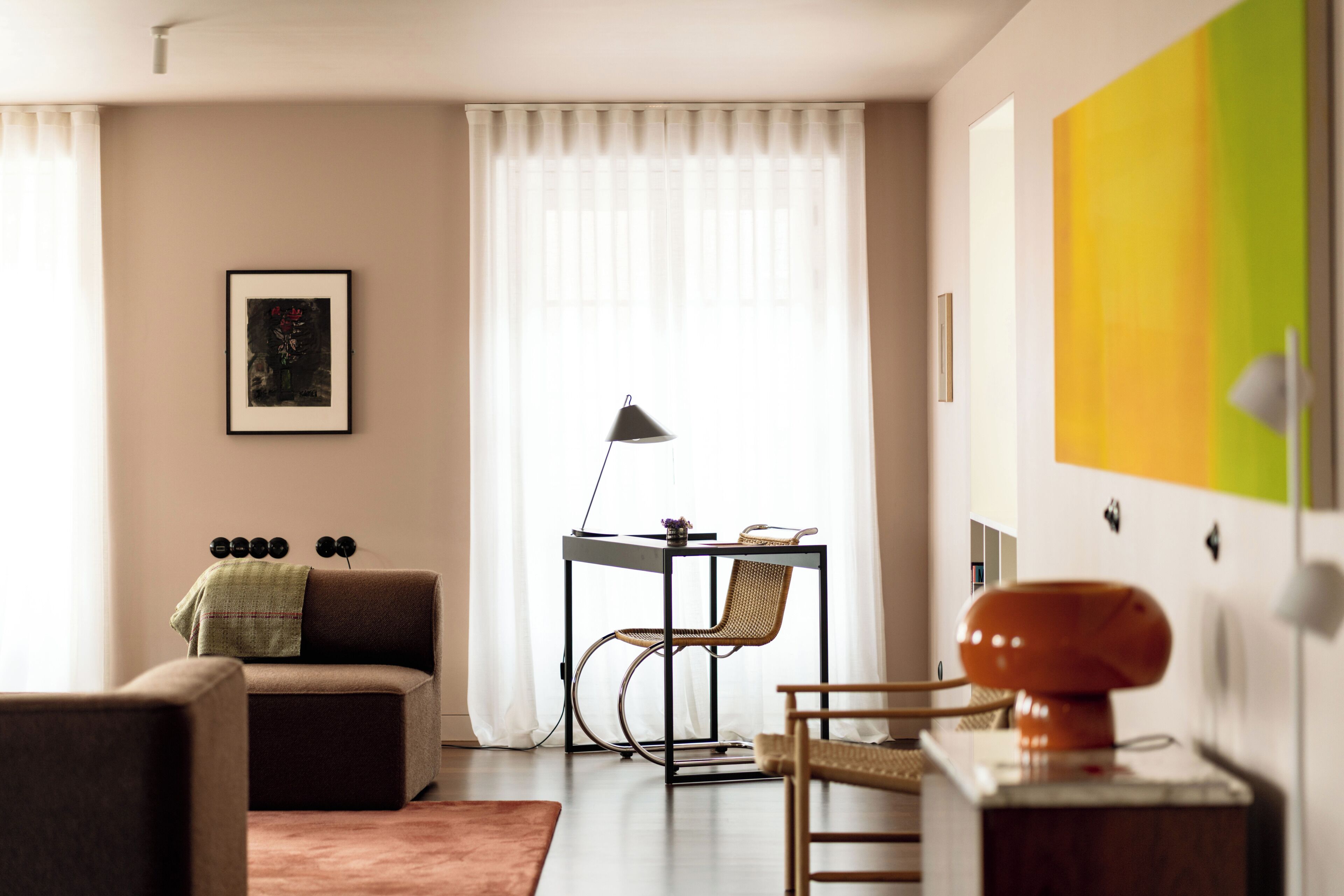 A living room with a sofa, a dining table with a chair, a lamp, and a painting on the wall.