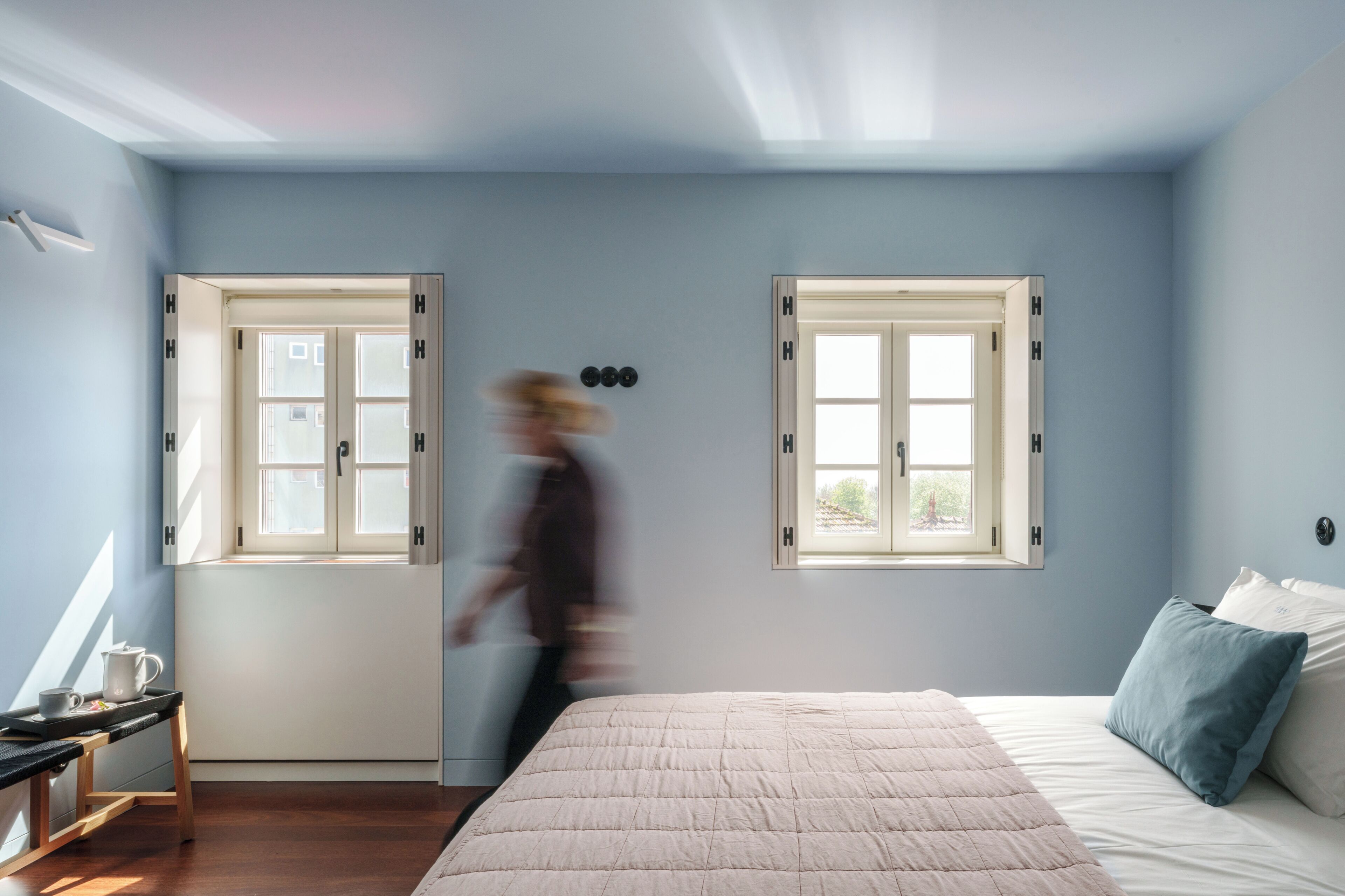 A bedroom with a bed, two windows, a nightstand, and a lamp.