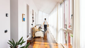 A hallway with a checkered floor, a sofa, a table with a vase, and a window with curtains.